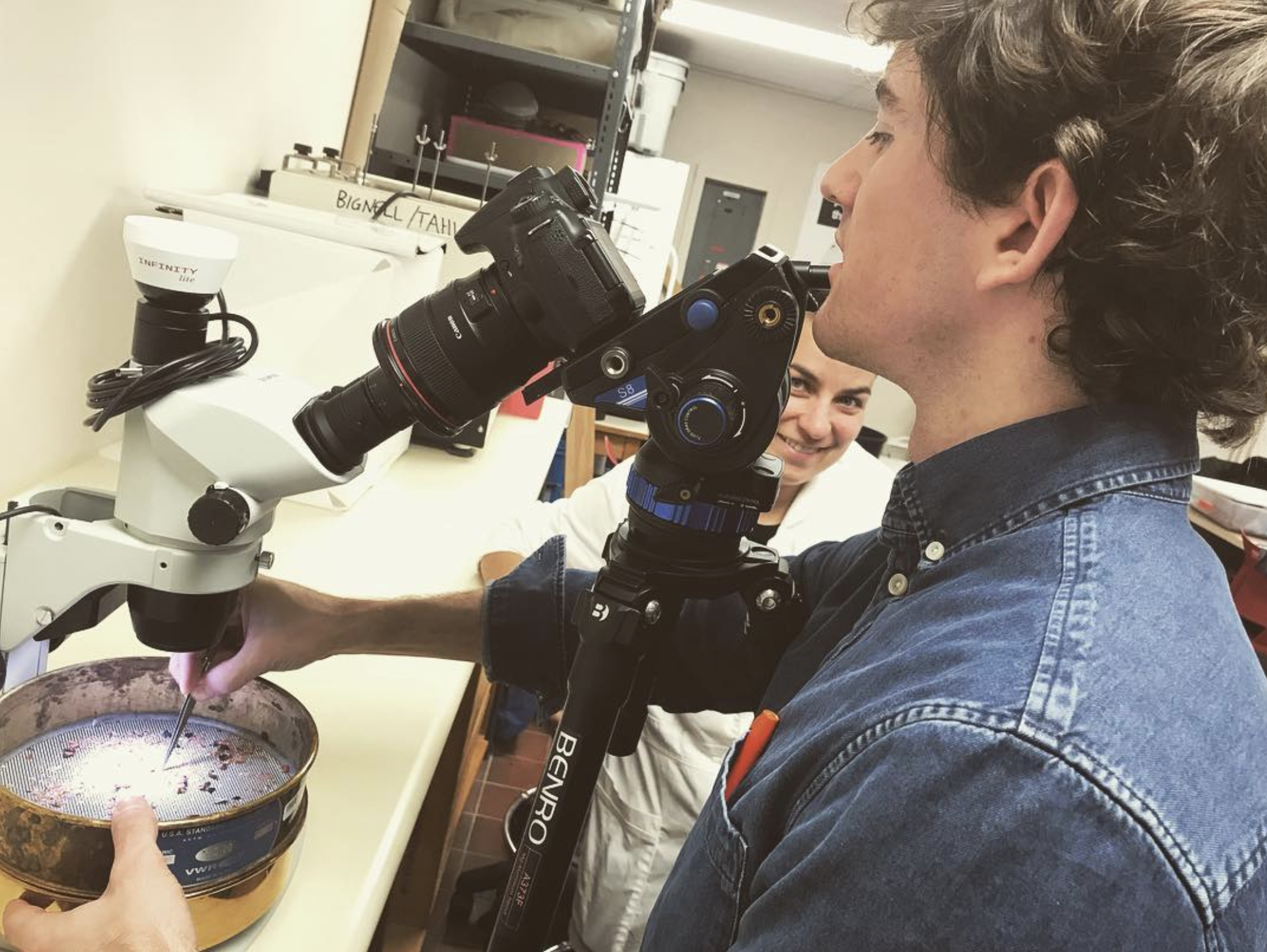 A man looks through a camera, through a microscope, at a sieve.